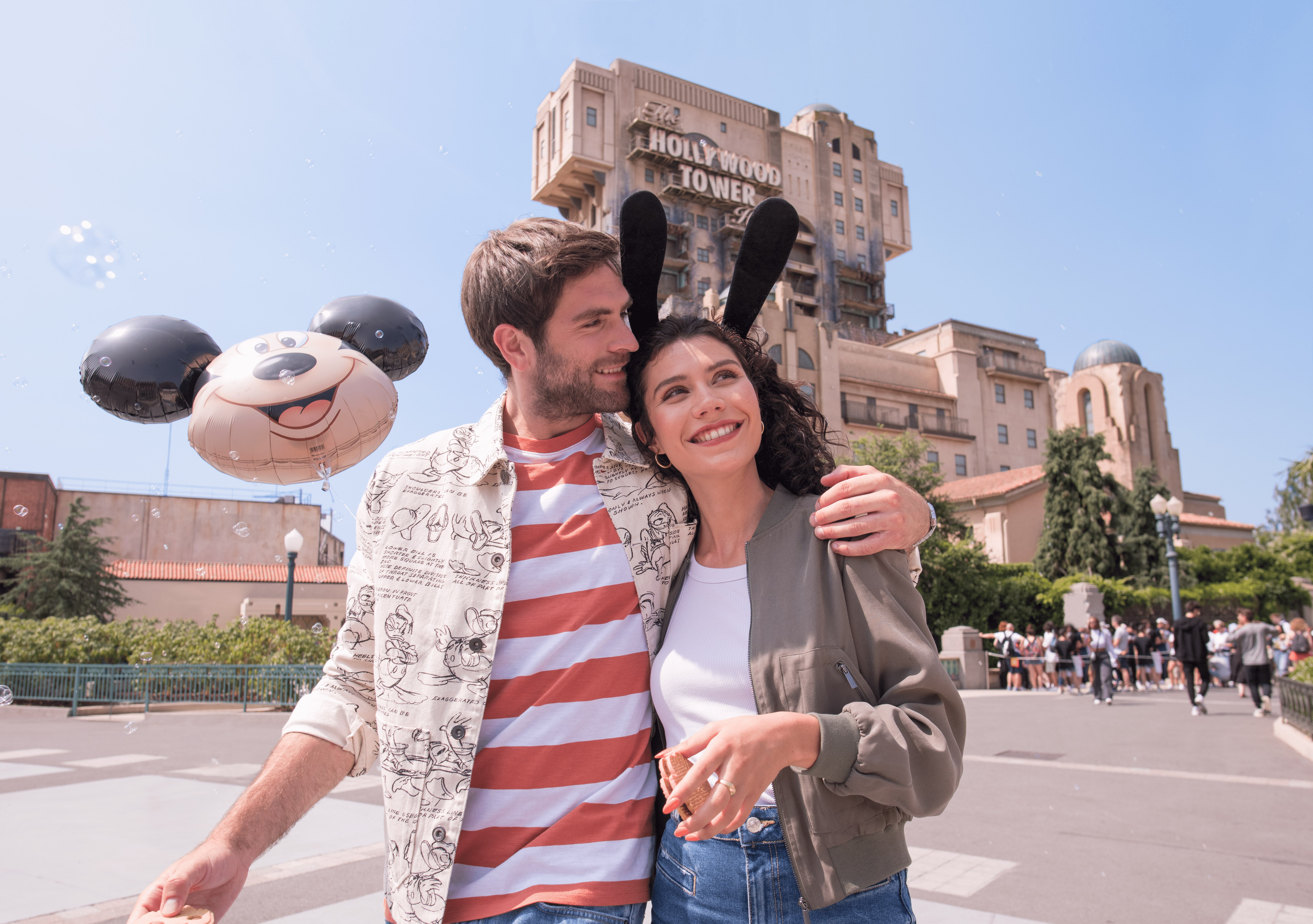 A couple embracing in front of The Twilight Zone Tower of Terror at Walt Disney Studios® Park, holding a Mickey Mouse balloon